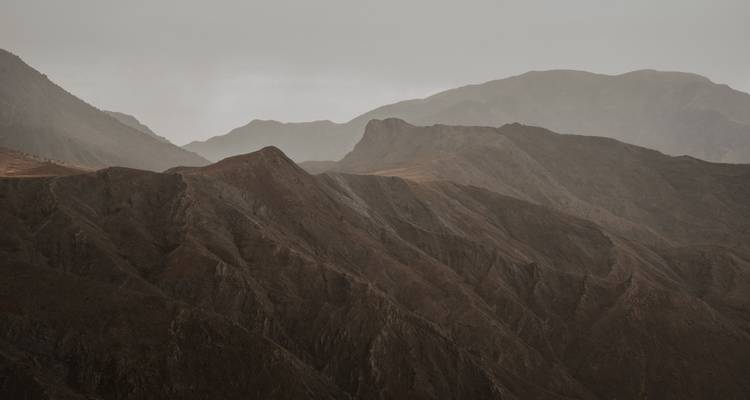 Líneas de crestas caprichosas y escarpadas de montañas áridas que se desvanecen en la niebla bajo un cielo gris.