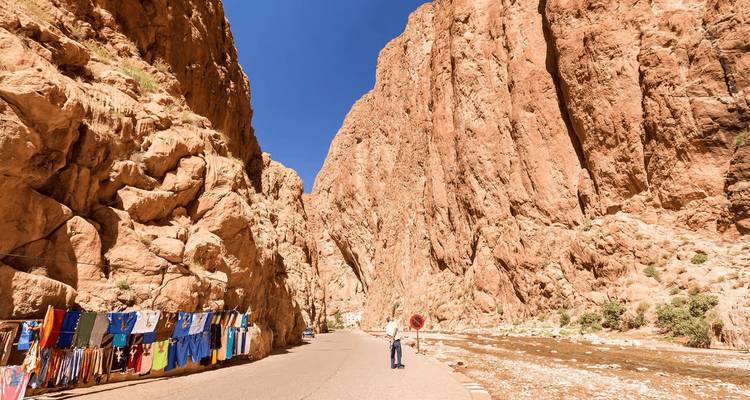 Carretera serpenteando a través de las imponentes paredes de piedra caliza naranja del Desfiladero del Todra con puestos locales colgando ropa