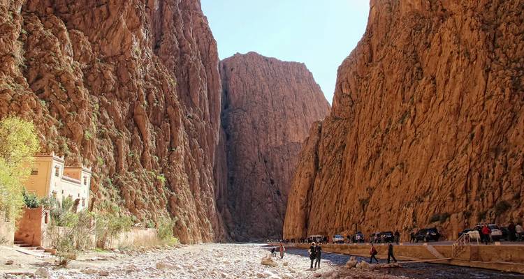 Los visitantes exploran el lecho rocoso del río bajo las paredes verticales del Desfiladero de Todra