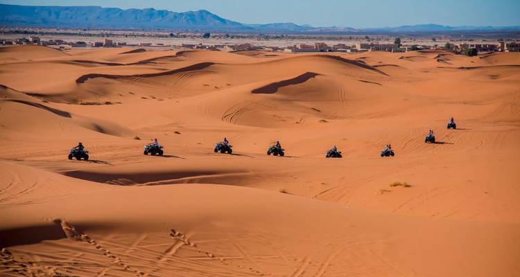 Larga fila de motociclistas de cuatrimoto tallan senderos a través de dunas infinitas cerca de un asentamiento desértico