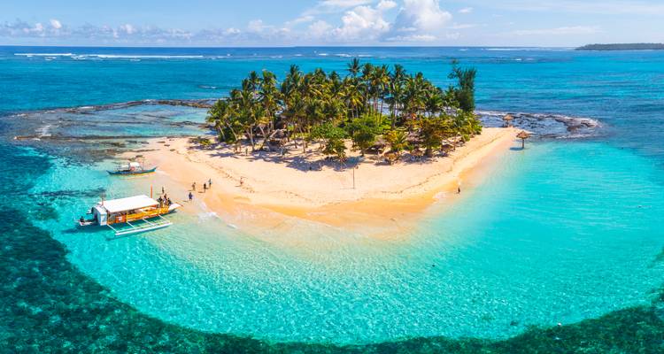 Piepklein met palmbomen bedekt zandeiland omringd door elektrisch-blauwe lagune en boten.