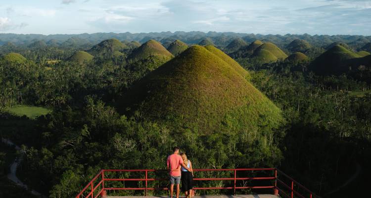 Stel bewondert eindeloze groene Chocolate Hills vanaf verhoogd rood uitkijkplatform.