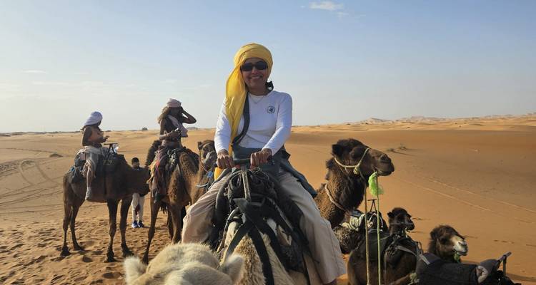 Mujer sonriente lidera una fila de jinetes de camellos a través de las doradas dunas de Erg Chebbi.