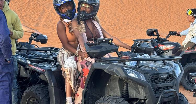 Dos mujeres con cascos están sentadas en un vehículo todo terreno listas para conducir por la arena cerca de Merzouga.