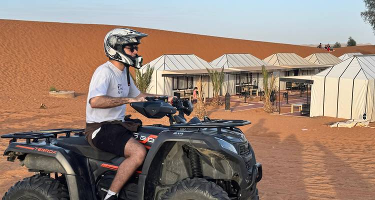 Un jinete en un cuatrimoto se detiene cerca de tiendas de lujo del desierto instaladas junto a dunas doradas.