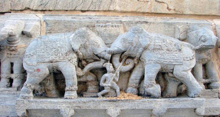 Ancient stone carving of elephants locked in combat on a temple base.