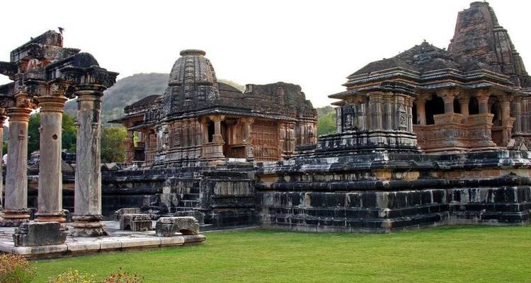 Historic stone temples and pillars surrounded by manicured grass in Rajasthan.