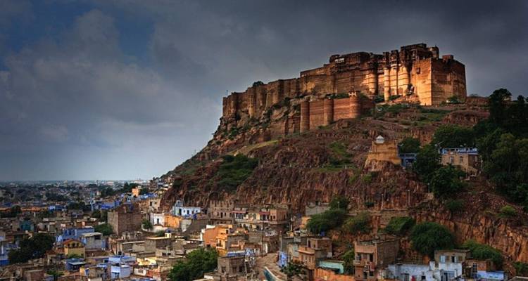 Mehrangarh Fort dramatically perched above the blue city of Jodhpur under moody skies.