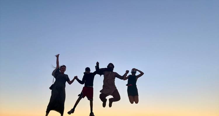 Silhouetten von vier Personen beim Springen vor einem pastellfarbenen Abendhimmel.