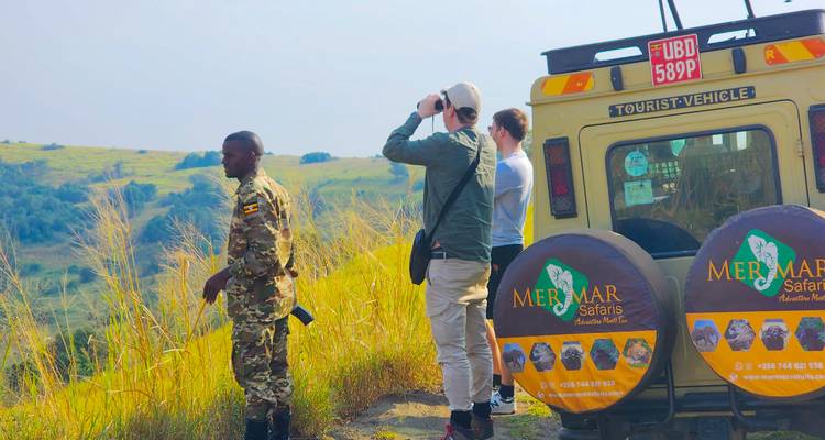 Guía y viajeros de pie junto a un vehículo de safari con vista a colinas cubiertas de hierba