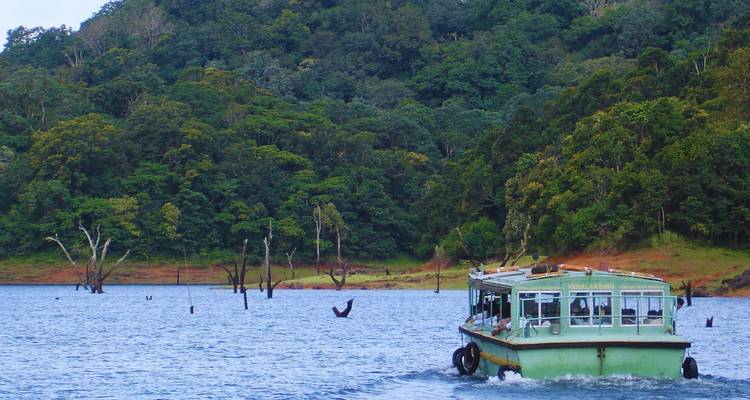 Ein Ausflugsboot gleitet über einen See, der von dichtem Regenwald im Periyar-Nationalpark umgeben ist.