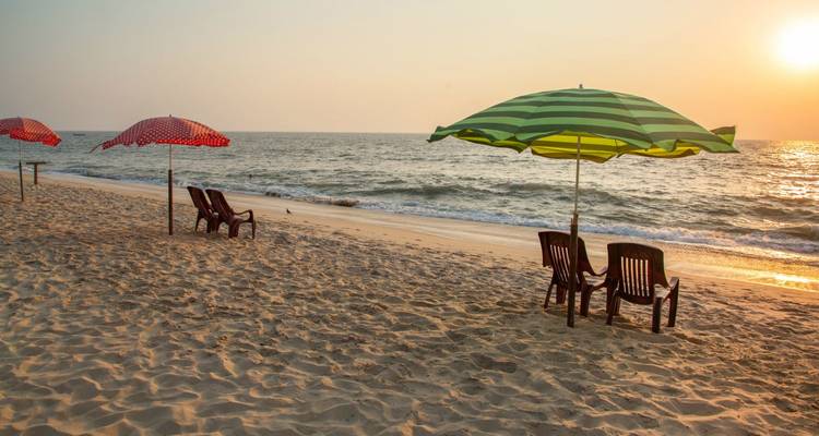 Leere Plastikstühle und gestreifte Sonnenschirme blicken während eines sanften Strandsonnenuntergangs auf das Arabische Meer.