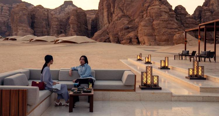 Two guests relax on modern outdoor sofas amid dramatic sandstone cliffs at dusk.