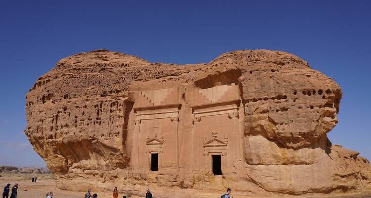 Twin rock-cut tombs stand in the desert with small visitors at their base.