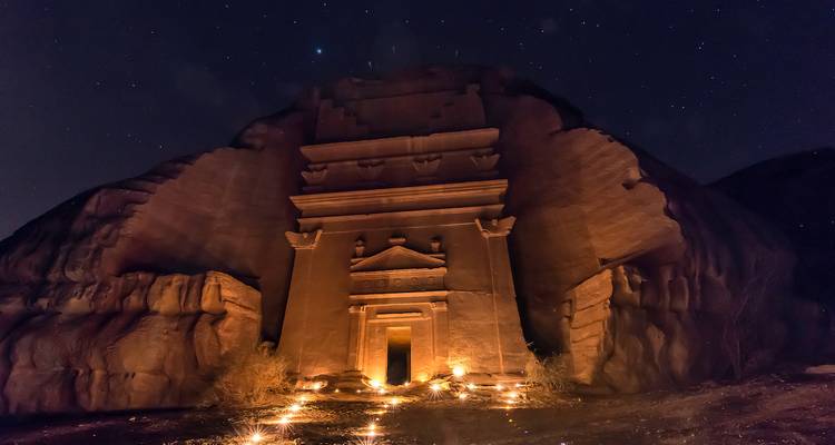A Nabataean tomb illuminated by soft candlelight under a star-filled night sky.
