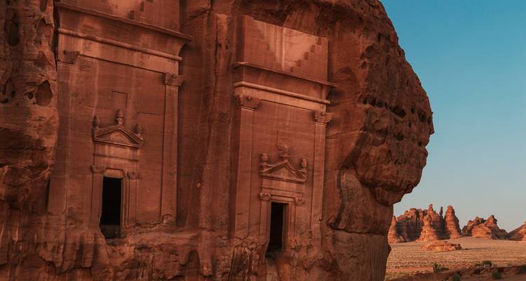 Twin rock-cut tomb façades set into a rugged cliff face under a clear sky.