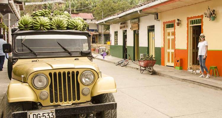 Une jeep chargée de bananes vertes est garée dans une rue colorée de petite ville.