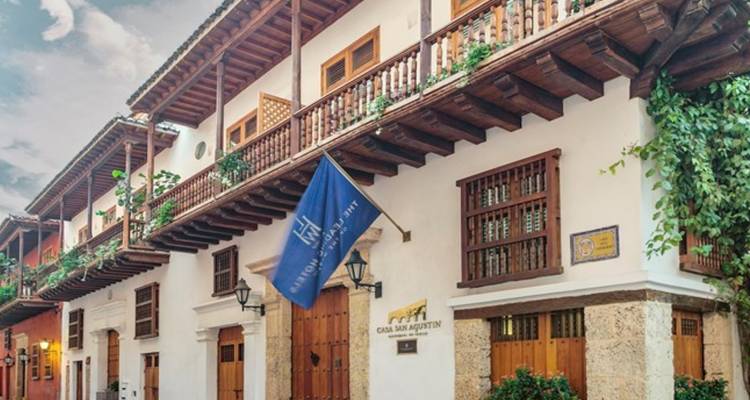 Élégant bâtiment blanc de style colonial avec balcons en bois, base en pierre et un drapeau bleu indiquant Casa San Agustin.