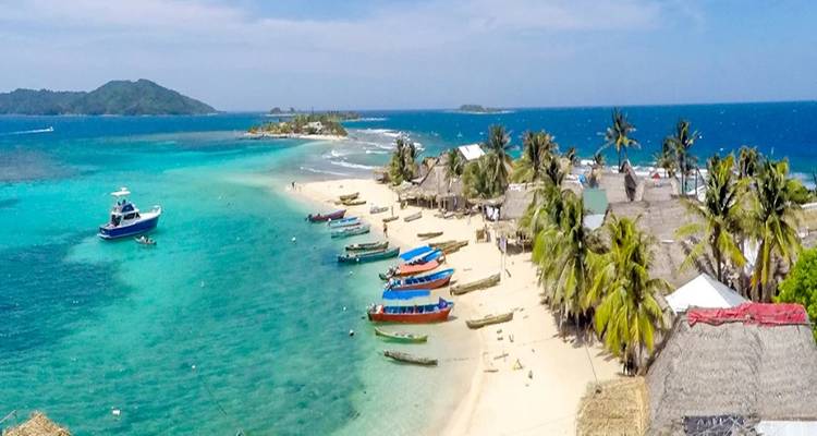 Vue panoramique aérienne d'une petite île des Caraïbes avec des plages de sable blanc, des bateaux de pêche colorés et des eaux turquoise.