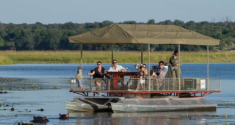 Tourists seated on a flat pontoon boat with canopy watching wildlife on a tranquil lagoon.