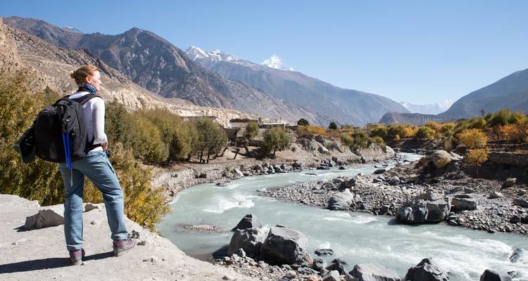 Eenzame trekker kijkt uit over een turquoise rivier die zich door een ruige bergvallei slingert