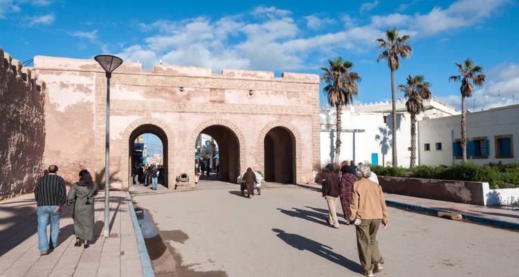 Stenen poort met drie bogen in Essaouira met palmbomen en voetgangers