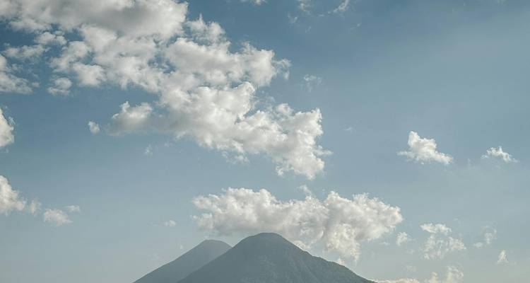 Conos volcánicos gemelos se elevan a través de nubes dispersas contra un cielo guatemalteco azul pálido.