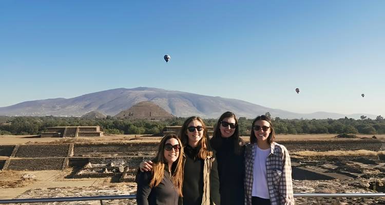Vier vrienden poseren met heteluchtballonnen die zweven boven Teotihuacans Piramide van de Zon op de achtergrond.
