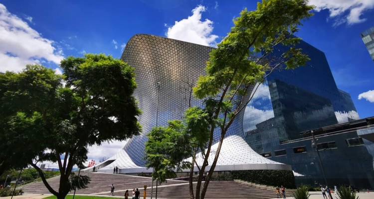De futuristische zilveren rondingen van Museo Soumaya glinsteren naast glazen wolkenkrabbers en groene bomen.