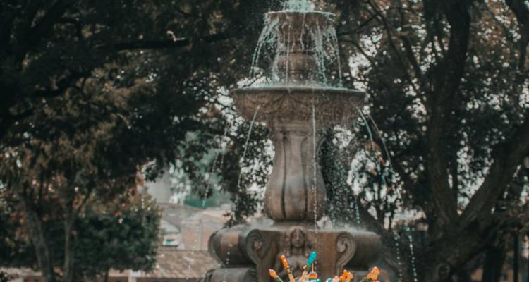 Een stenen fontein spat water tussen bladrijke bomen met vage kleurrijke speelgoed op de voorgrond.
