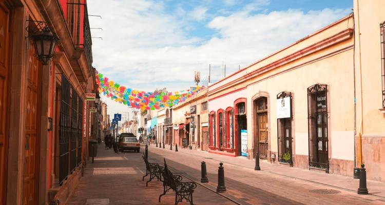 Charming pedestrian street with colorful banners hanging overhead, lined by restored colonial buildings under a bright sky.