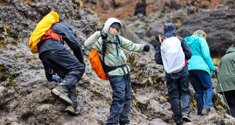 Excursionistas con equipo para la lluvia trepan sobre rocas volcánicas resbaladizas en una ladera brumosa.