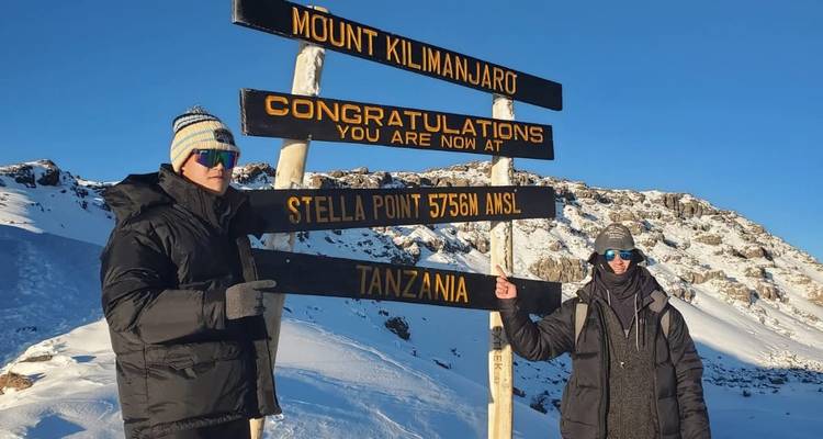 Dos escaladores posan junto al letrero de Stella Point 5756 m en el Kilimanjaro cubierto de nieve al amanecer.
