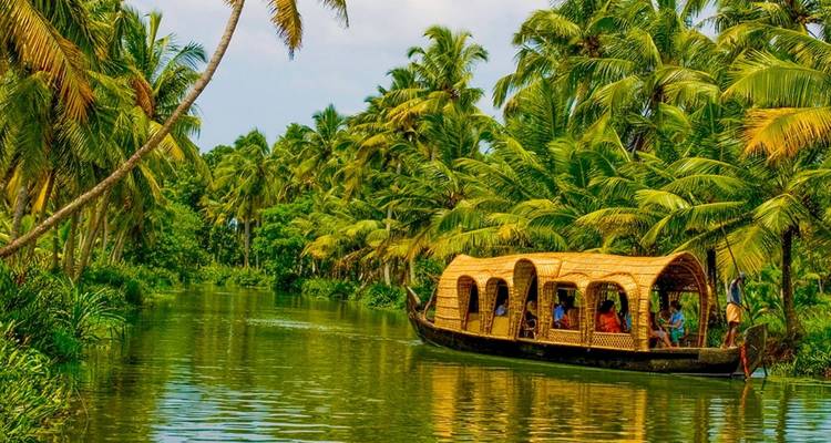 Traditionelles Kerala-Hausboot, das durch üppig grüne Backwaters fährt, die von sich neigenden Palmen gesäumt sind.