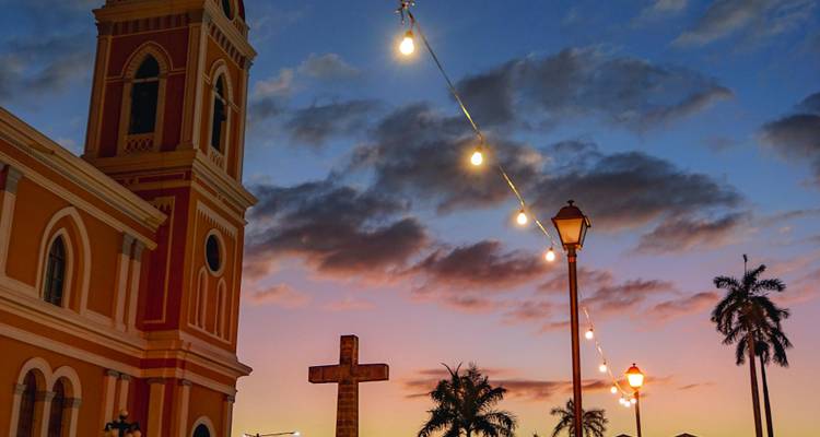 Colonial cathedral tower and palm trees silhouetted against a colourful sunset sky.