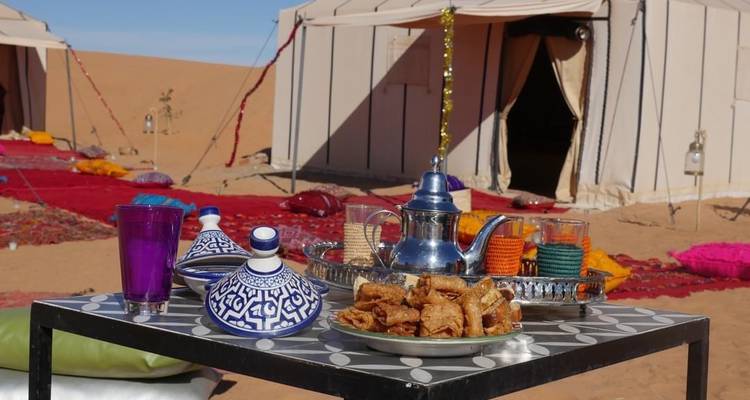 Service à thé et pâtisseries marocaines sur une table basse dans un campement du désert sablonneux.