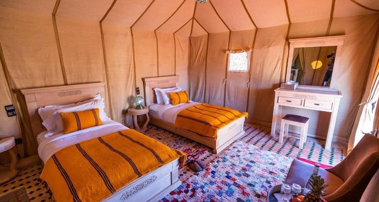 Intérieur de tente confortable avec lits jumeaux et textiles berbères colorés dans un camp de glamping du désert.