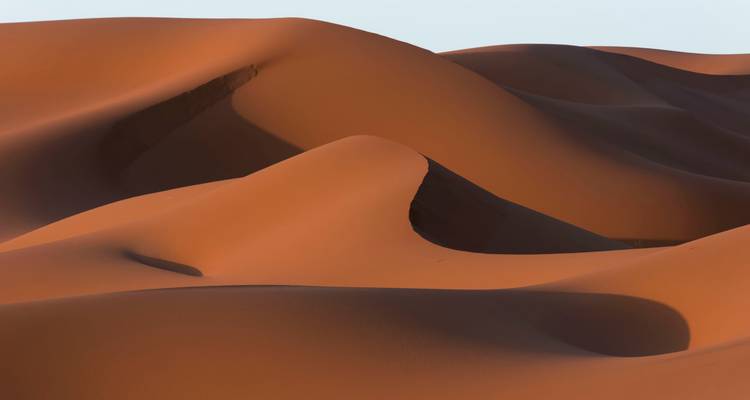 Primer plano abstracto de suaves dunas de arena naranja esculpidas bajo una luz suave.