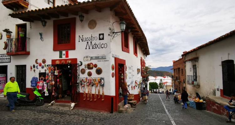 Kopfsteinpflasterstraße mit einer Souvenirladenfront mit der Aufschrift 'Nuestro México' und Menschen, die im kolonialen Taxco stöbern