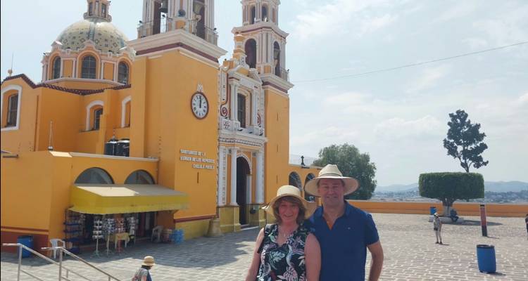Paar mit Sonnenhüten stehend vor der leuchtend gelben Kirche von Cholula mit Glockentürmen