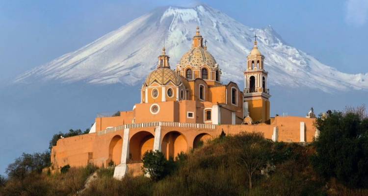 Ikonische Cholula-Kirche auf einem Hügel, eingerahmt vom schneebedeckten Vulkan Popocatépetl