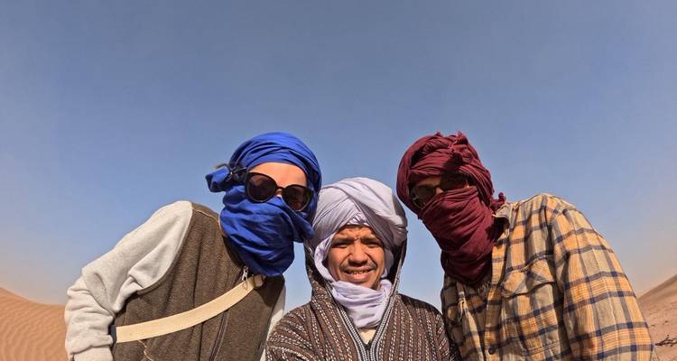 Selfie van drie reizigers die kleurrijke woestijnturbans dragen tegen een heldere blauwe lucht.