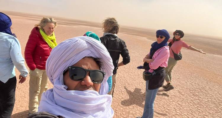 Reizigers met hoofddoeken staan op gebarsten woestijngrond tijdens een zandbeladen wind