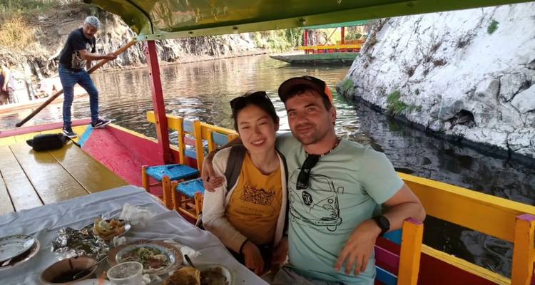 Una pareja disfruta de una comida en un barco pintado de colores brillantes que flota por canales bordeados de rocas.