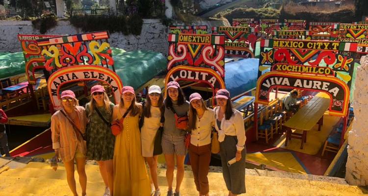 Grupo de amigos posa frente a coloridos botes de Xochimilco ornamentalmente pintados en el muelle.