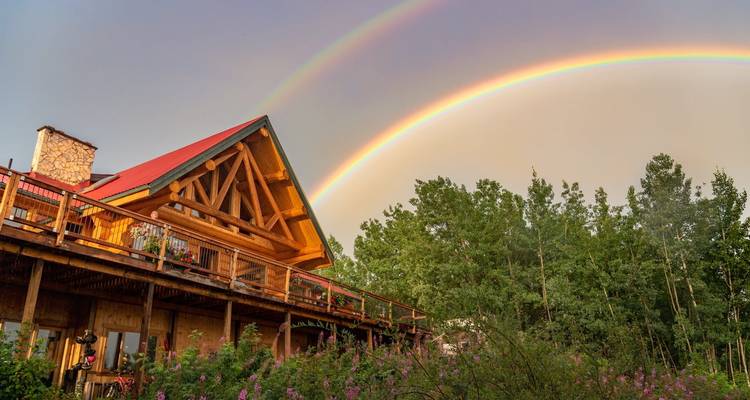Chalet rustique en bois sous un double arc-en-ciel éclatant avec de l'épilobe en fleurs au premier plan