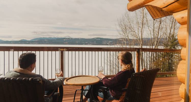 Couple profitant de boissons sur une terrasse en bois avec vue sur un lac gelé et des montagnes au loin