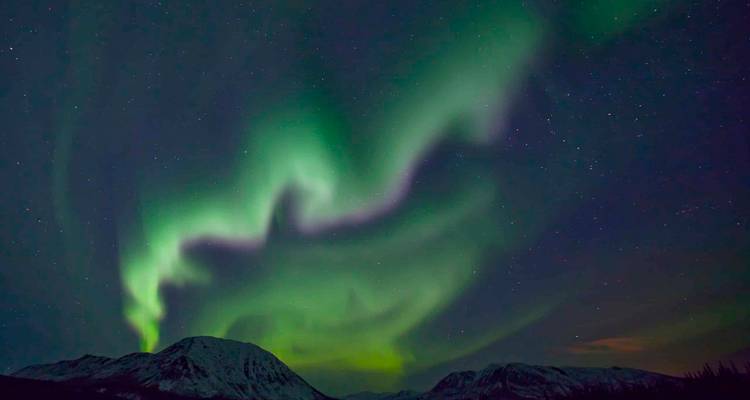 Aurore boréale d'un vert éclatant tourbillonnant dans le ciel nocturne au-dessus de montagnes enneigées