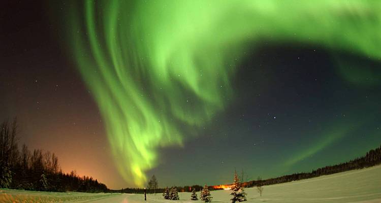 Rideau d'aurore verte spectaculaire au-dessus d'une plaine enneigée avec de faibles lumières de village à l'horizon