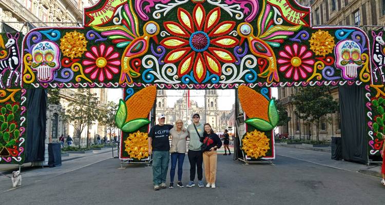 Vier reizigers die poseren onder een kleurrijke Día de Muertos bloemenboog op het Zócalo in Mexico City.